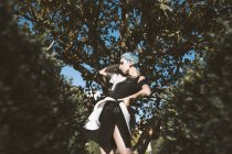 Знизу молода жінка в футуристичному вбранні, дивлячись на камеру, стоячи біля дерев у розмитому стані — стокове фото