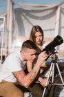 Donna elegante seduta sulle ginocchia fidanzato che guardando attraverso il telescopio al cielo vicino bolla hotel — Foto stock