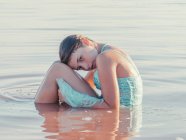 Задумчивая девушка в платье сидит в волнистой воде — стоковое фото