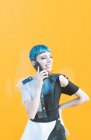 Junge Frau in futuristischem Kleid, die lachend Anrufe entgegennimmt, während sie vor einer knallgelben Wand steht — Stockfoto