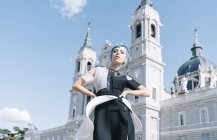 Junge Frau im trendigen futuristischen Kleid hält die Hand auf der Taille, während sie an einem sonnigen Tag auf der Stadtstraße steht — Stockfoto