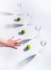 Female hand with green ripe limes near clear glasses of water on white background — Stock Photo