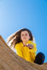 Portrait of brunette woman in yellow sweatshirt giving hand on sandstone rock on blue sky background — Stock Photo