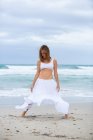 Привлекательная женщина в белом наряде танцует на песке рядом с морем — стоковое фото