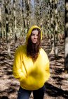 Portrait de jeune femme en sweat-shirt jaune debout sur fond de bosquet — Photo de stock