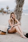 Молода приваблива жінка з довгим волоссям розслабляється на березі моря і розмовляє мобільним телефоном в літній день — стокове фото