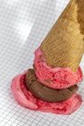 Waffle cornet with chocolate and strawberry ice cream fallen on squared paper — Stock Photo