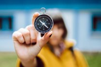 Cheerful blur young woman holding retro compass near face while standing on blurred background of countryside house — Stock Photo