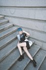 Giovane donna con i capelli corti blu indossa abito informale alla moda e posa su gradini di strada — Foto stock