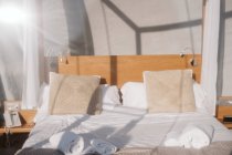 Made-up bed with white linen and beige pillows under transparent roof on sunny daytime — Stock Photo