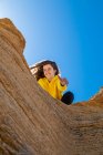 Ritratto di donna bruna in felpa gialla che dà mano su roccia arenaria su sfondo cielo blu — Foto stock