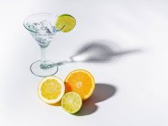 Glass of drink full of ice cubes and sliced orange, lime and lemon on white background — Stock Photo