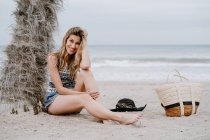 Portrait of young beautiful blonde seductive woman sitting down on beach and looking at camera — Stock Photo