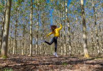 Молодая женщина в желтой толстовке прыгает в лесу — стоковое фото