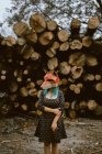 Anonymous female in paper fox mask covering full head looking away and standing with crossed arms on background with stack of logs. Concept of negative human impact on wildlife habitat — Stock Photo
