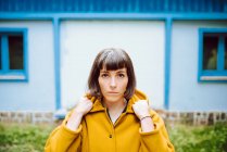 Junge Frau in gelbem warmen Mantel lächelt und blickt in die Kamera, während sie vor grauer Wand steht — Stockfoto