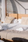 Geschminktes Bett mit weißer Bettwäsche und beigen Kissen unter transparentem Dach am sonnigen Tag — Stockfoto