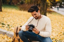 Handsome young photographer in autumn park watching photos on camera — Stock Photo