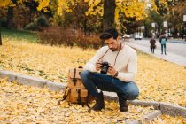 Schöner junger Fotograf im Herbstpark, der sich Fotos vor der Kamera ansieht — Stockfoto