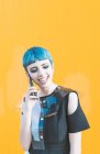 Jeune femme en robe futuriste riant et répondant à un appel téléphonique tout en se tenant contre un mur jaune vif — Photo de stock