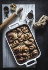 From above tray with fresh homemade cinnamon buns and wooden rolling pin on white marble board — Stock Photo
