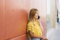 Jeune femme parlant sur téléphone portable appuyé sur le mur rouge — Photo de stock