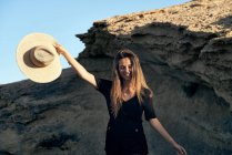 Junge lächelnde Frau blickt mit Hut auf felsige Küste — Stockfoto