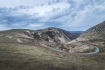 Route étroite sinueuse passant sur des pentes de collines herbeuses par temps nuageux en campagne — Photo de stock