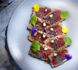 Зверху смачні апетитні свіжі шматочки тунця татакі з зеленим листям на тарілці — стокове фото