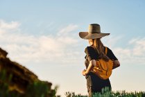 Вид ззаду на туриста-жінку в солом'яному капелюсі та рюкзаку в природі — стокове фото