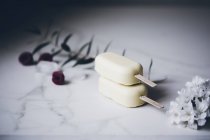 Ghiaccioli di gelato al cioccolato bianco impilati su una superficie di marmo decorata con fiori — Foto stock