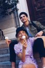 Fröhliche junge attraktive Frau und Freund essen Eis, während sie draußen sitzen — Stockfoto