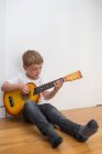 Kleiner blonder Junge spielt Spielzeuggitarre — Stockfoto