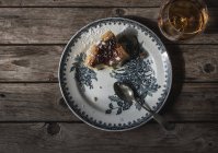 Top view of slice of cottage cheese baked pudding served on plate and glass of cognac on wooden table — Stock Photo