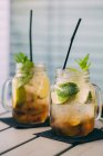 Deux cocktails mojito préparés avec du citron vert, de la menthe, du rhum, de la soude et de la glace dans des pots de maçon sur la table — Photo de stock