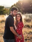 Чоловік обіймає усміхнену вагітну дружину на фоні мальовничого зеленого парку в сонячний день — стокове фото