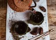Servant un thé parfumé savoureux dans une théière en argile tasse et des dates douces sur plateau blanc décoré de feuilles de thé sur fond en bois — Photo de stock