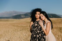 Woman with closed eyes leaning on shoulder of friend while standing in field with dry grass near hills — Stock Photo