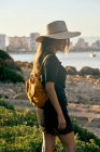 Женщина-туристка в соломенной шляпе и рюкзаке стоит рядом с пляжем — стоковое фото