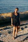Jeune femme attrayante profitant du soleil avec les yeux fermés sur la plage et tenant chapeau — Photo de stock
