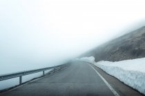 Asphalt road through snowy mountainous terrain on misty day — Stock Photo