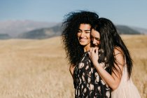 Woman leaning on shoulder of friend while standing in field with dry grass near hills — Stock Photo