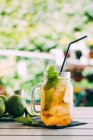 Coquetel de mojito preparado com limão, hortelã, rum, refrigerante e gelo em pote de pedreiro na mesa ao ar livre — Fotografia de Stock