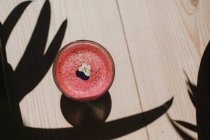 Bolla schiumosa gustoso profumato frullato rosa decorato con fiore in vetro su tavolo di legno con ombra — Foto stock