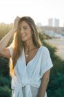 Jovem mulher atraente em roupas brancas sorrindo e olhando para a câmera ao ar livre — Fotografia de Stock