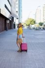 Young female tourist in sunglasses with suitcase walking on street — Stock Photo