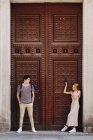 Jovem casal alegre e brincalhão em roupas casuais posando na frente da bela porta velha durante o namoro ao ar livre — Fotografia de Stock