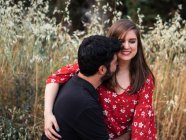 Uomo che abbraccia sorridente moglie incinta seduta in grembo sullo sfondo del pittoresco parco verde nella giornata di sole — Foto stock