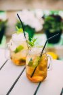 Two mojito cocktails prepared with lime, mint, rum, soda and ice in mason jars on table outdoors — Stock Photo