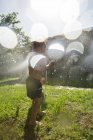 Anonymous little children in swimwear running around and splashing water from garden hose at each other — Stock Photo